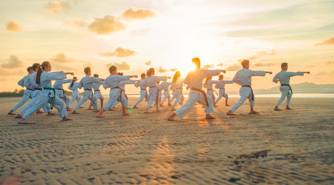 Group of martial artists practicing on a beach during sunset, demonstrating various forms