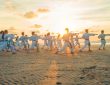 Group of martial artists practicing on a beach during sunset, demonstrating various forms