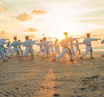 Group of martial artists practicing on a beach during sunset, demonstrating various forms