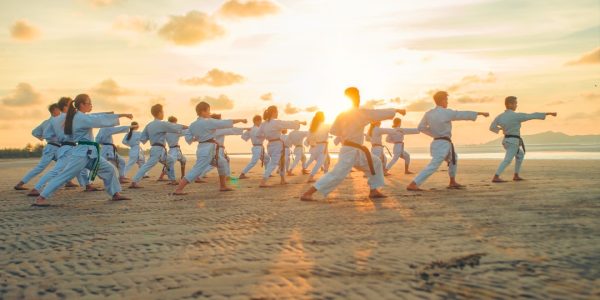Group of martial artists practicing on a beach during sunset, demonstrating various forms