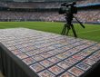 A table covered with sports trading cards, positioned in a stadium setting with a camera nearby.