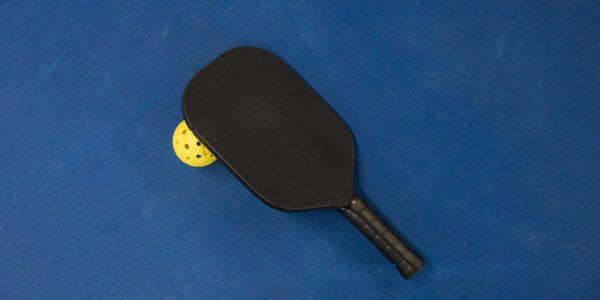 Black pickleball paddle resting on a yellow pickleball on a blue surface